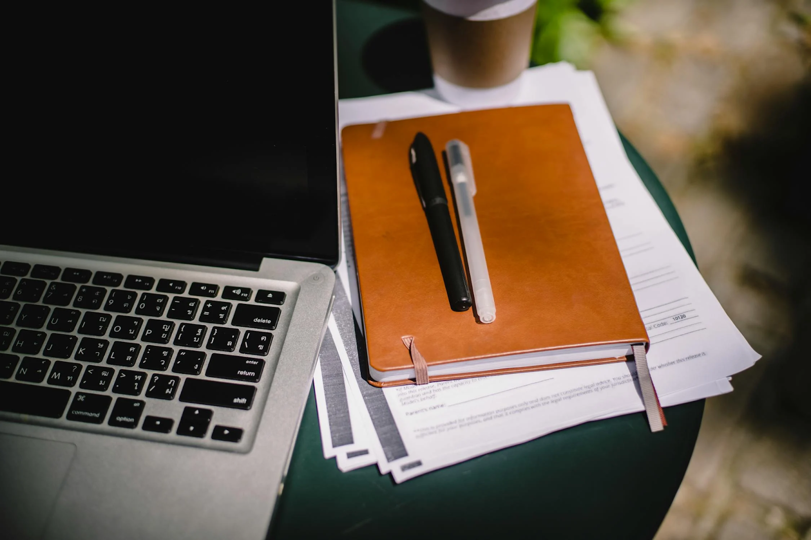 A laptop sits on a desk next to a notebook and pens