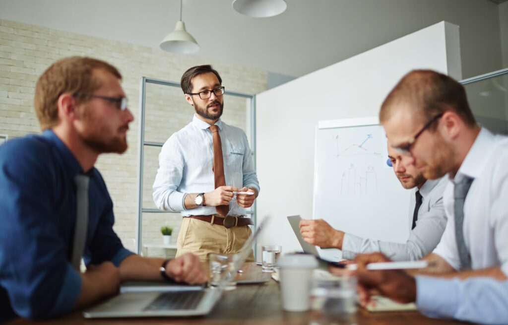 HR professional leading a discussion on essential HR skills with colleagues during a business meeting, with charts and data on a whiteboard in the background.