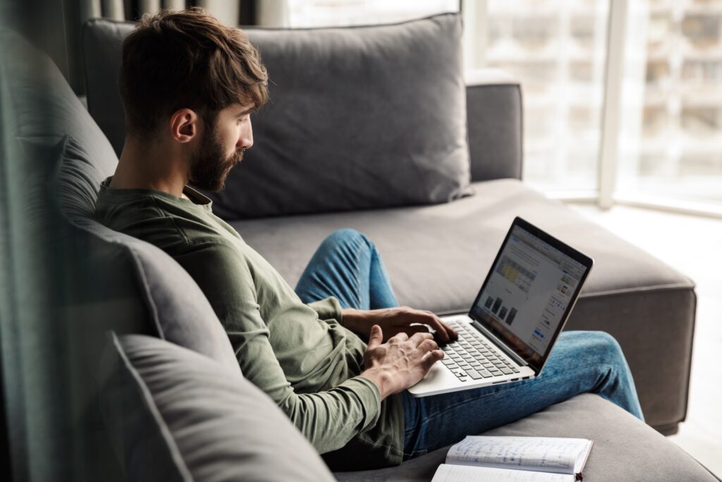 A male employee works on his laptop from home on his couch