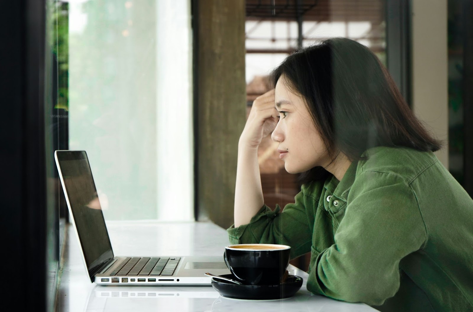 A woman with a cup of coffee sitting at a table looking at a computer deciding what HR certification courses online she should take