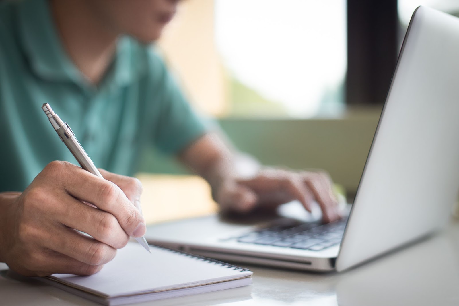 A man writing notes while studying online